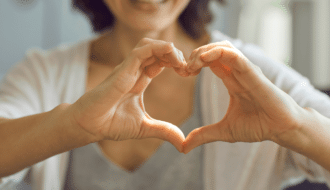 Close-up of a woman forming a heart shape with her hands, symbolizing love and gratitude.