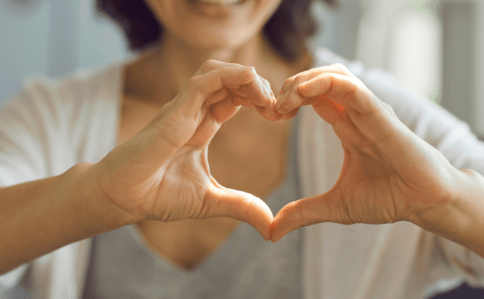 Close-up of a woman forming a heart shape with her hands, symbolizing love and gratitude.