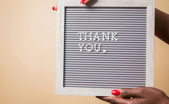 Hands holding a framed sign with the words "Thank You" against a beige background.