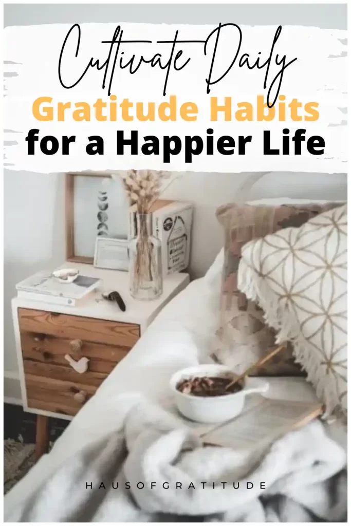 A cozy bedroom scene focused on a wooden nightstand with dried flowers in a vase, a bowl, and books, next to a bed with a grey throw and a patterned pillow. Text overlay reads "Cultivate Daily Gratitude Habits for a Happier Life."