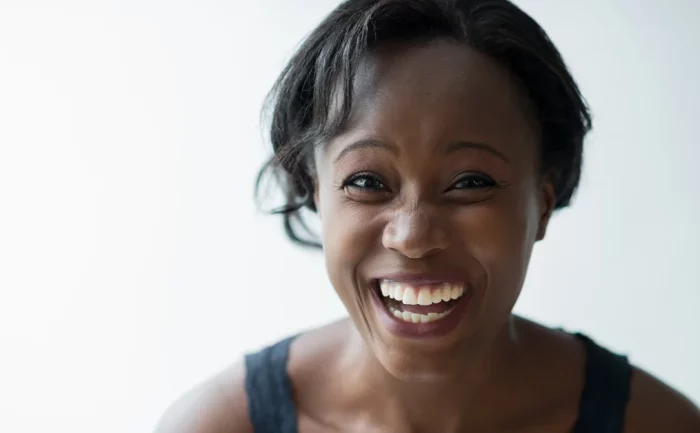 Joyful African American woman smiling broadly with a clear, glowing complexion, against a bright white background.