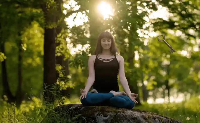 Woman meditating on a rock in a sunlit forest with a floating key overhead symbolizing unlocking life's mysteries